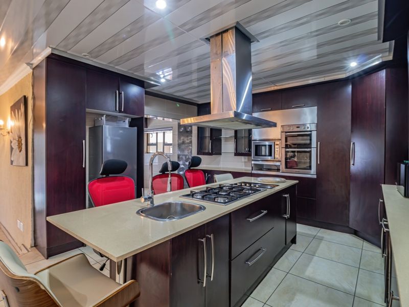 Modern kitchen featuring dark wood cabinetry, a central island with a gas hob and sink, stone countertops, and integrated stainless steel appliances.