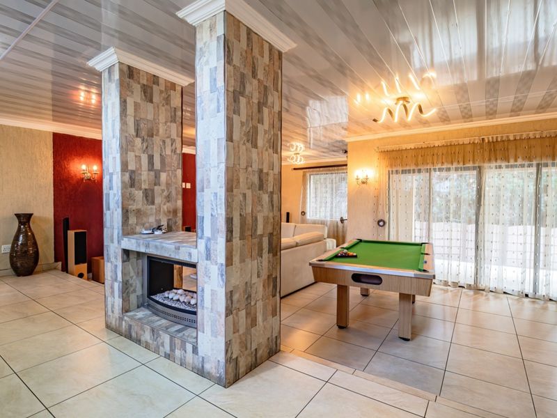 Spacious living area featuring a central stone-clad fireplace, tiled flooring, and glossy ceiling panels, with sliding glass doors providing access to the outdoors.