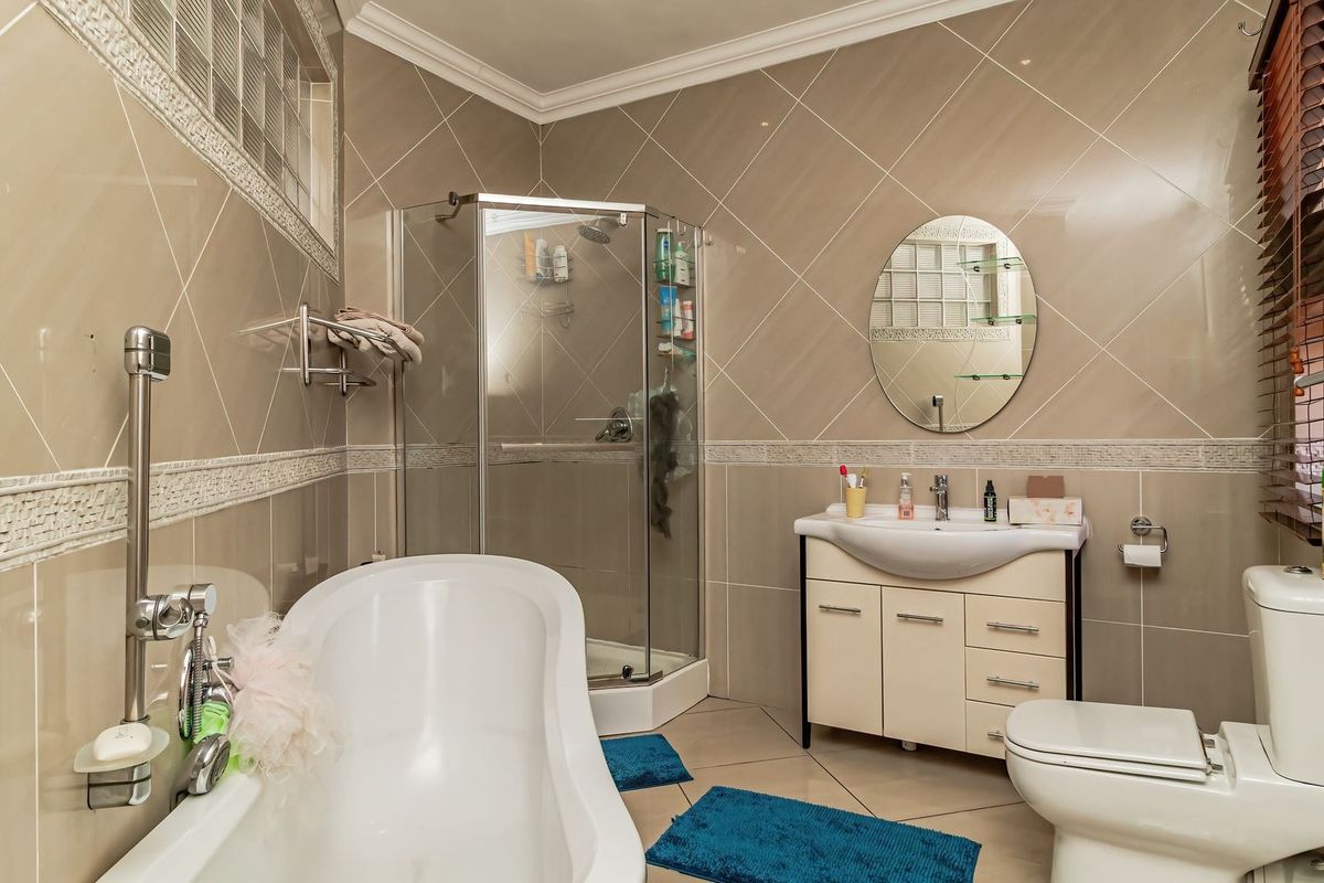 A well-maintained bathroom featuring a freestanding bathtub, corner shower, vanity unit, and toilet, finished with neutral wall tiles and crown molding.