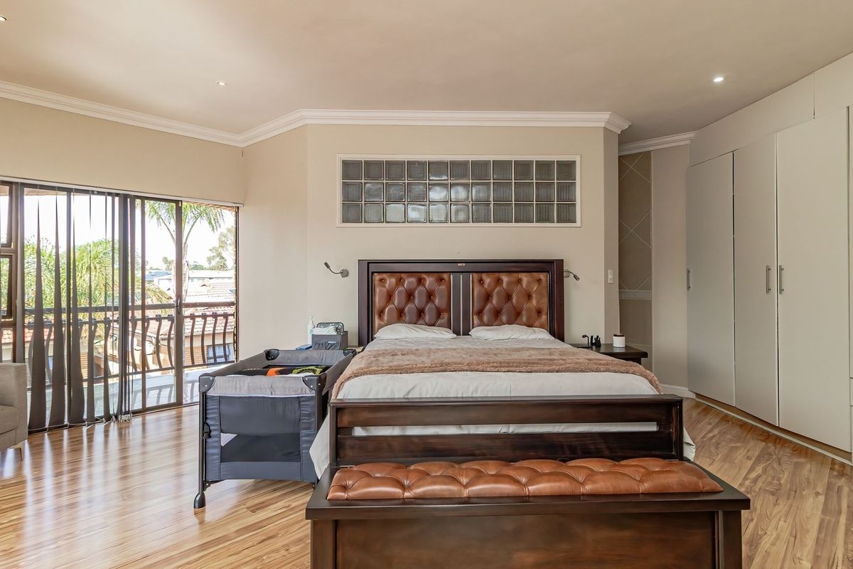 Spacious bedroom featuring laminate flooring, extensive built-in cupboards, a decorative glass block feature window, and sliding door access to a private balcony.