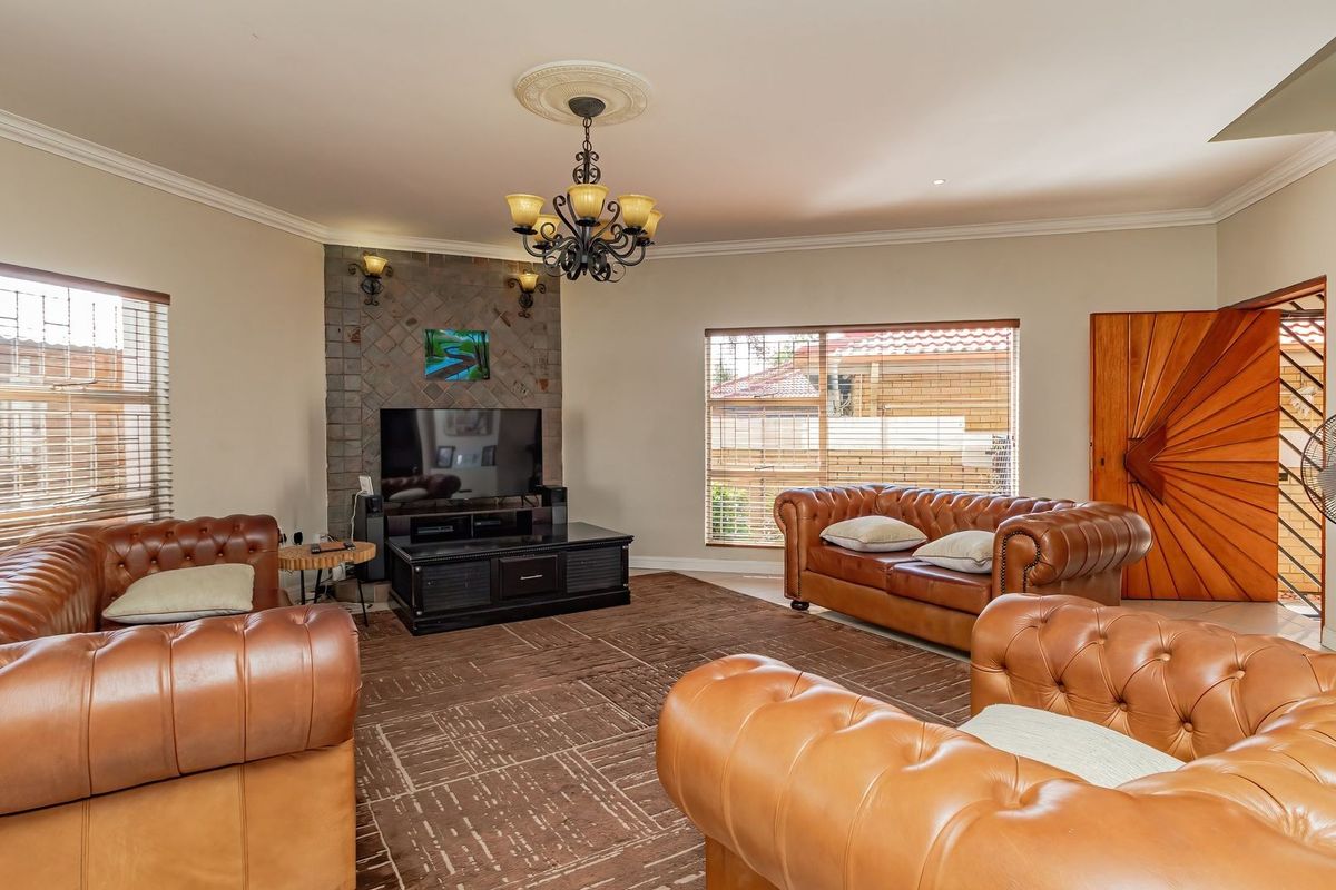 Spacious living room featuring a stone-clad fireplace, decorative ceiling rose with chandelier, and large windows providing ample natural light.