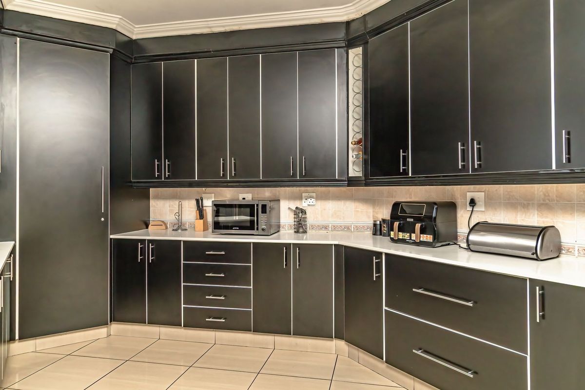 A modern kitchen featuring dark cabinetry, light stone countertops, tiled backsplash, and neutral floor tiles, offering a clean and functional workspace.
