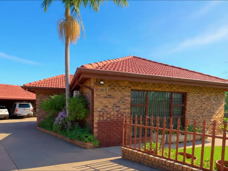Front view of a face brick house featuring a tiled roof, attached carport, and secure metal fencing along the front garden.