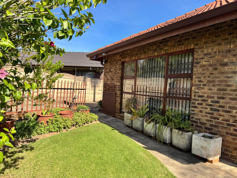 A well-maintained rear exterior view of a face brick house featuring a neat lawn, concrete pathway, and secure window treatments.