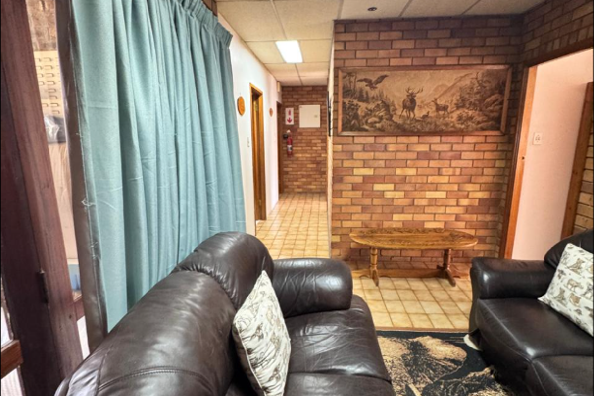 Living area featuring exposed brick walls, tiled flooring, and a drop ceiling, with access to an adjacent hallway.