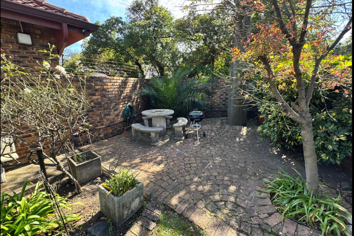 A private rear garden area featuring established trees, brick paving, and a secure brick boundary wall with electric fencing.