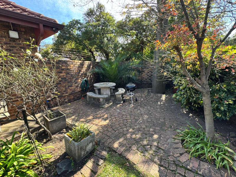 A private rear garden area featuring established trees, brick paving, and a secure brick boundary wall with electric fencing.