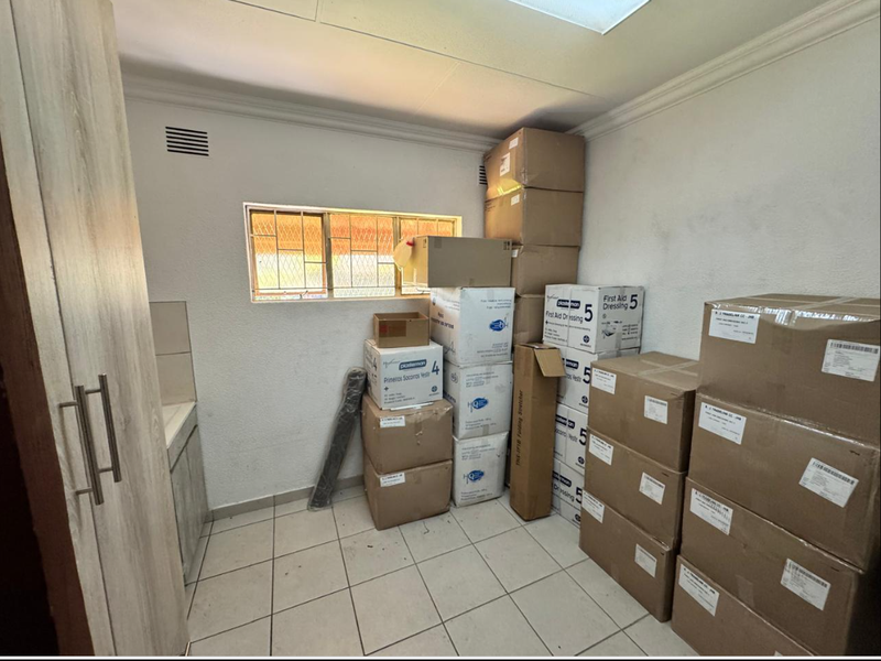 A functional laundry room featuring tiled flooring, built-in cabinetry, and a window with security bars, currently utilized for storage.