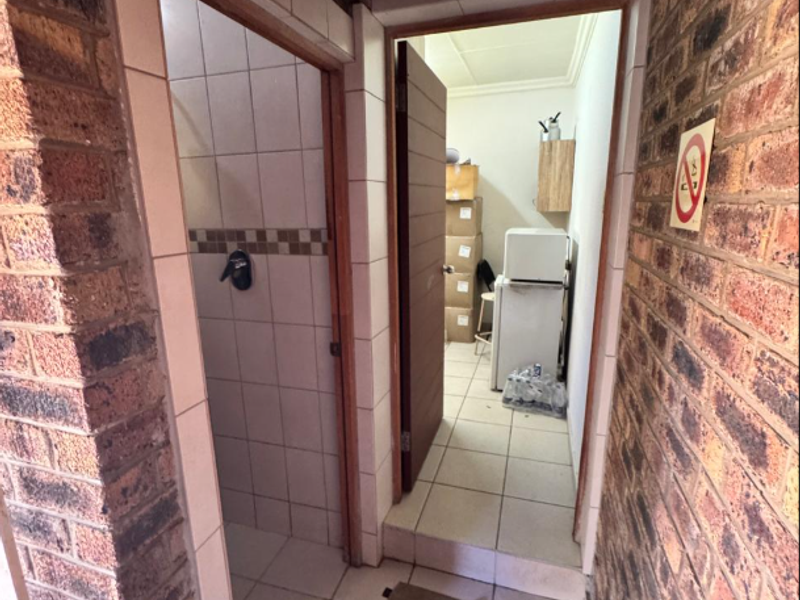 A utility area featuring exposed brick walls and tiled flooring, providing access to a small shower room and an adjacent storage or utility space.
