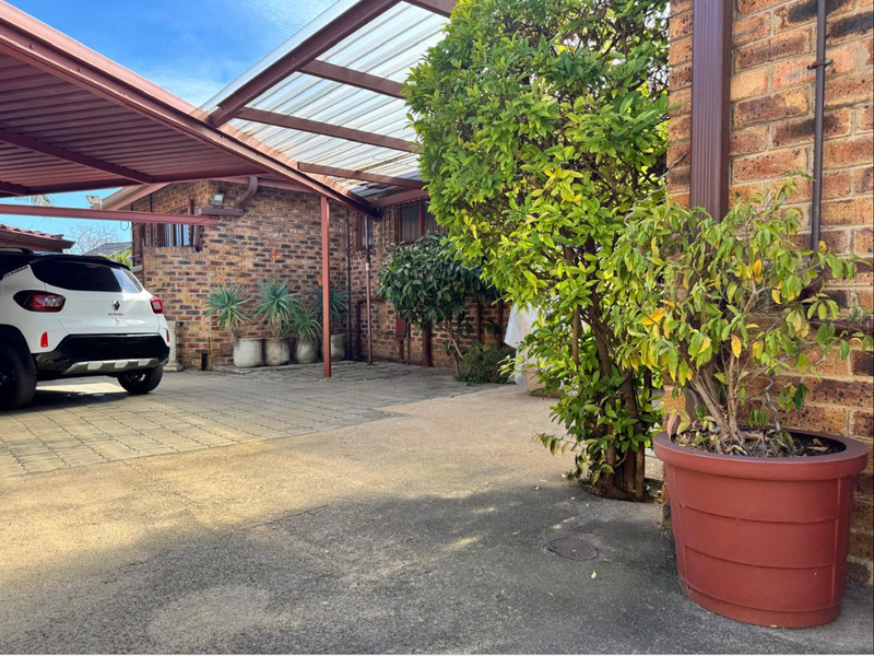 A functional front exterior area featuring a covered carport, brick facade, and paved driveway space.