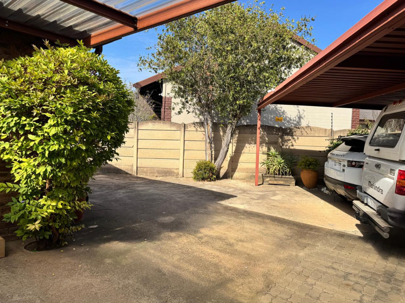 A paved driveway area featuring a covered carport structure and a precast concrete boundary wall.