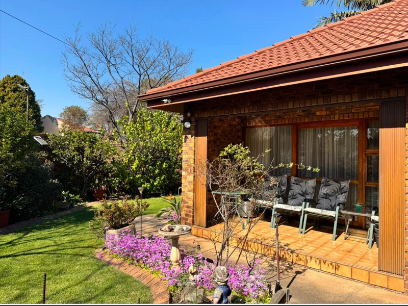 A covered brick patio featuring tiled flooring and sliding glass doors, overlooking a well-maintained garden area.