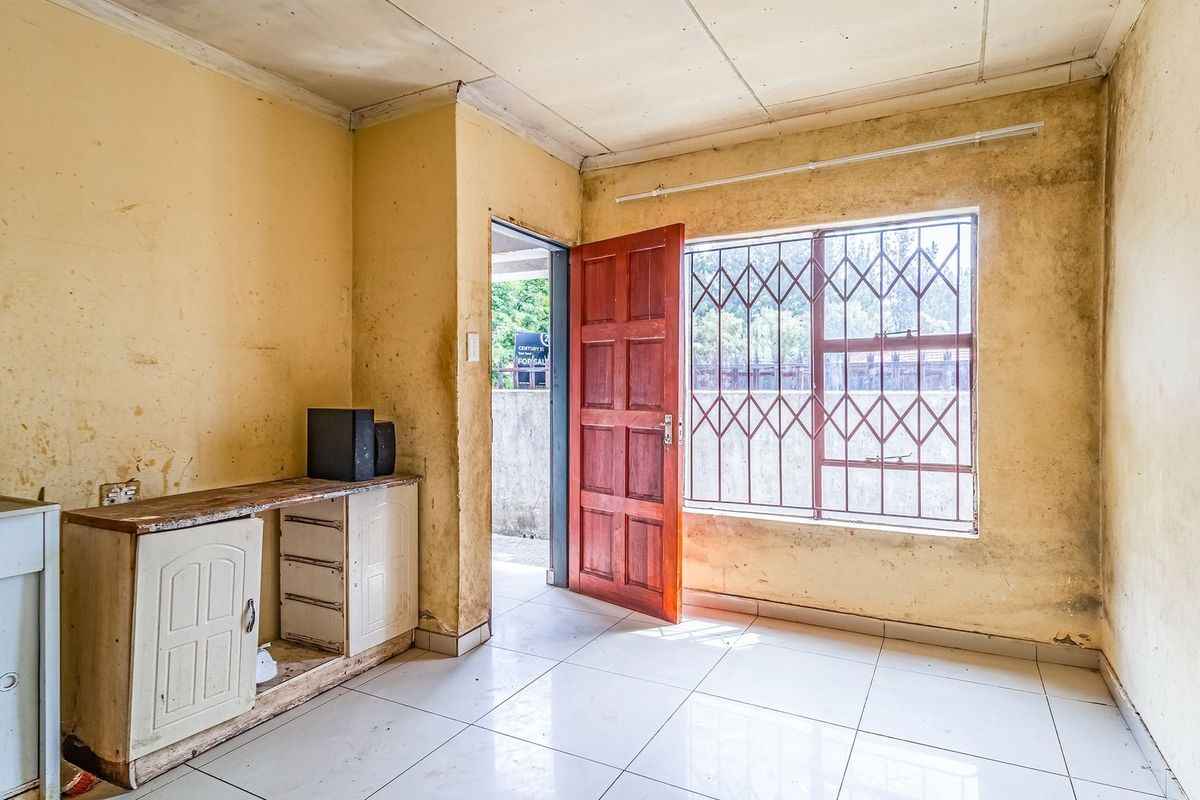 An empty living area featuring tiled flooring, security bars on the window, and built-in cabinetry, requiring cosmetic updates and wall repairs.