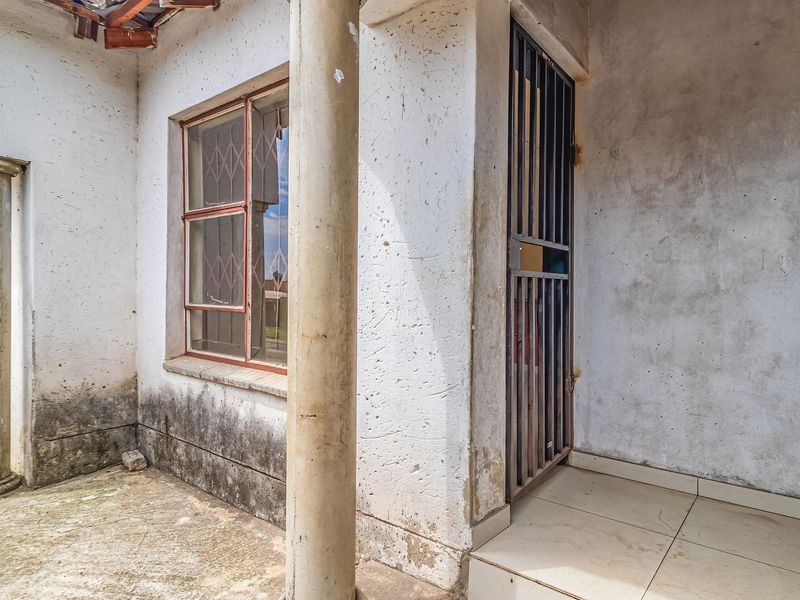 A covered patio area featuring concrete columns, tiled flooring, and security gates, currently showing significant signs of wear and weathering.