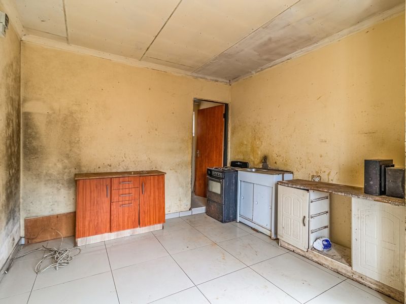 A basic kitchen area featuring tiled floors, a sink, and built-in cabinetry, currently in need of significant renovation and cosmetic repair.