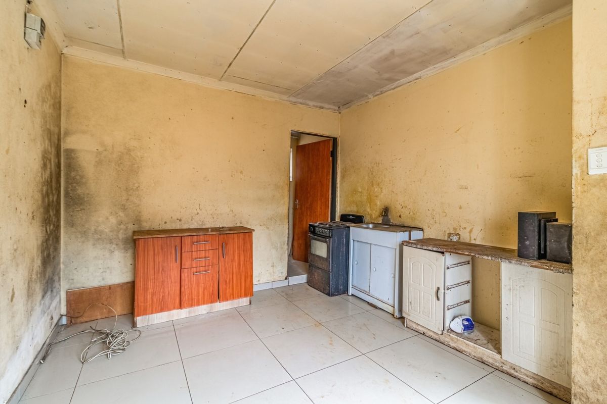 A basic kitchen area featuring tiled floors, a sink, and built-in cabinetry, currently in need of significant renovation and cosmetic repair.