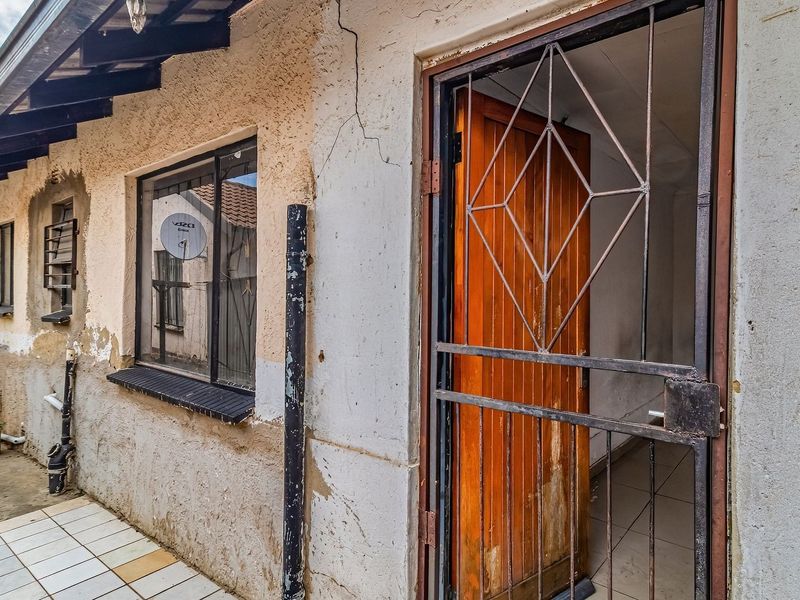 Rear exterior view showing a tiled patio area, security gate, and weathered wall finishes requiring maintenance and repair.
