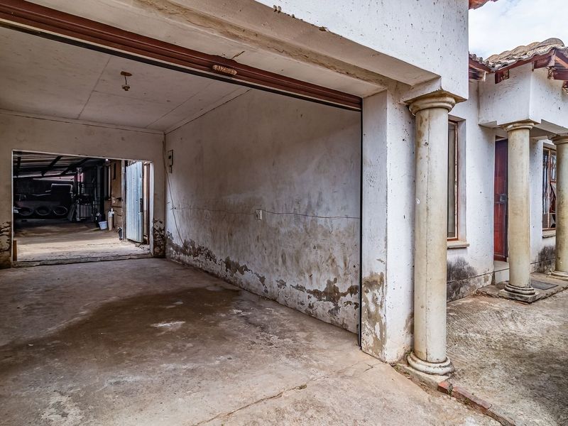 An open-plan garage area featuring concrete flooring and structural columns, showing significant signs of wear and damp on the exterior walls.