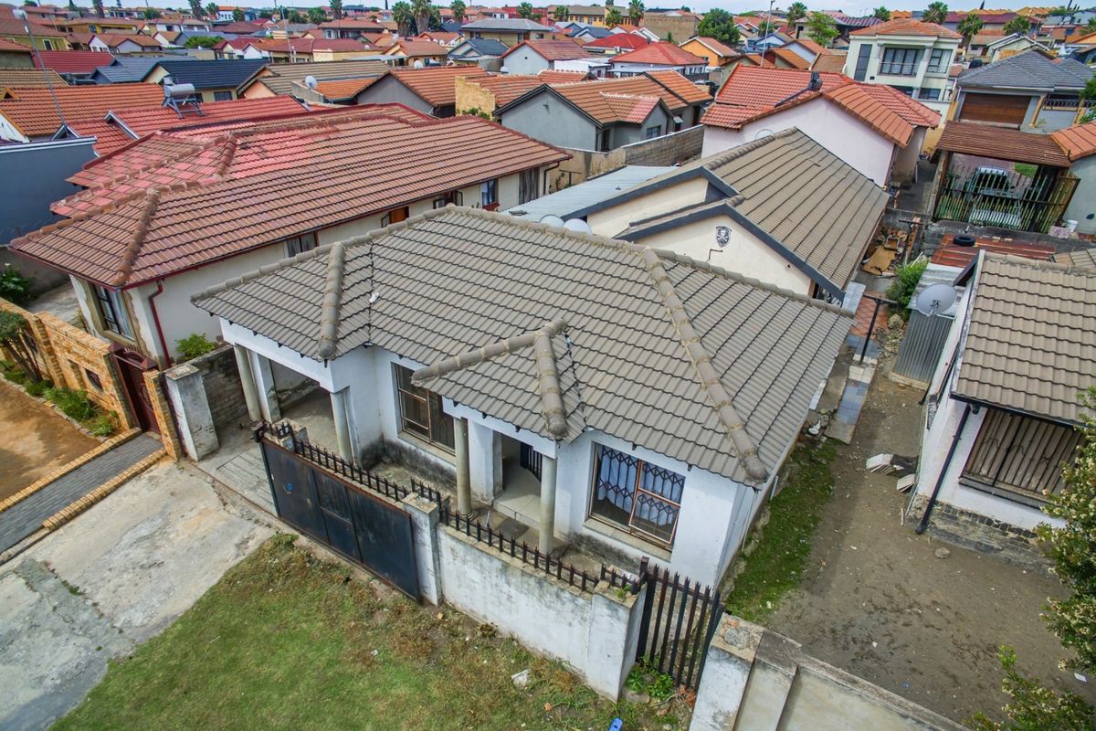 Aerial view of a residential property featuring a tiled roof, perimeter wall with metal gate, and security bars on windows in a suburban neighborhood.