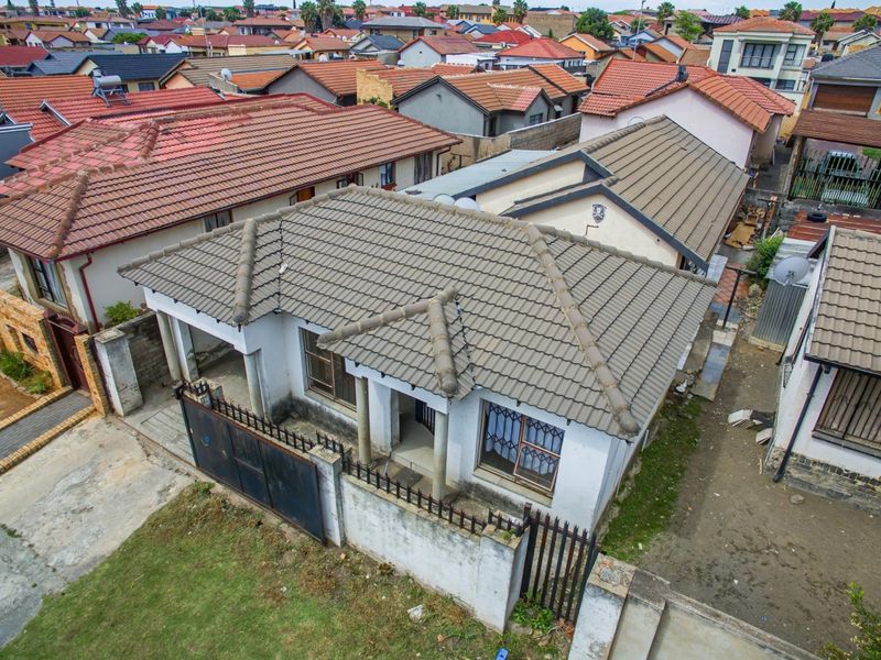 Aerial view of a residential property featuring a tiled roof, perimeter wall with metal gate, and security bars on windows in a suburban neighborhood.