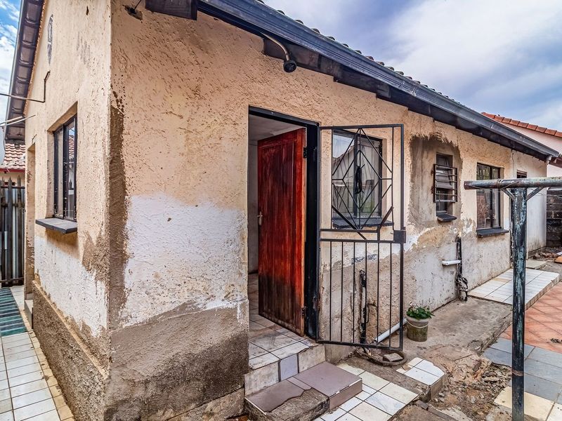 Rear exterior view of the property showing a weathered facade with peeling plaster, security gate, and tiled patio area requiring maintenance.