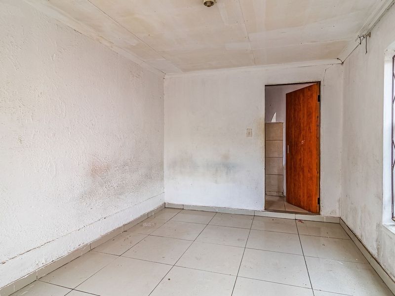 An empty bedroom featuring tiled flooring, a window with security bars, and a wooden door leading to an adjacent space.