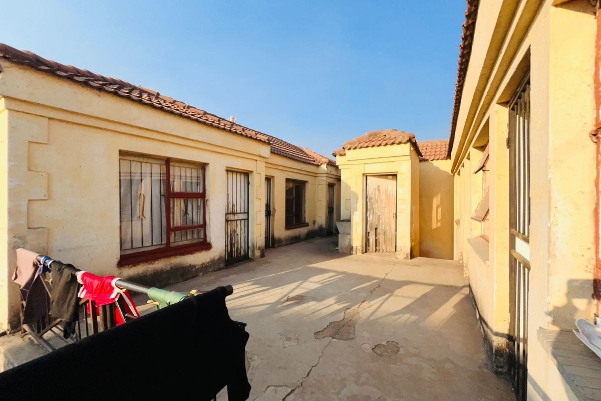 A rear courtyard area featuring weathered exterior walls, tiled roofing, and cracked concrete paving, requiring maintenance and cosmetic updates.