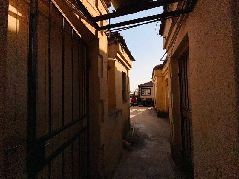 A narrow exterior passage between residential structures featuring stucco walls, metal security gates, and a concrete walkway.