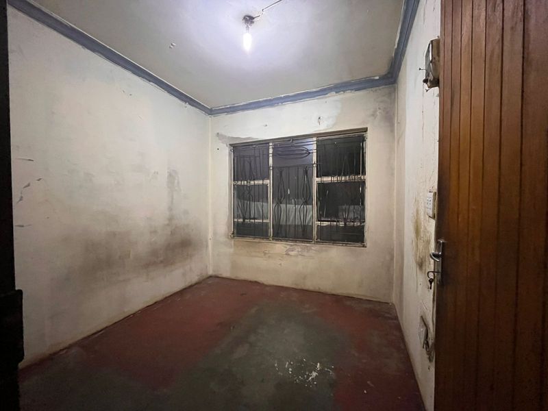 An empty bedroom featuring security bars on the window, requiring significant renovation and cosmetic updates to restore the space.