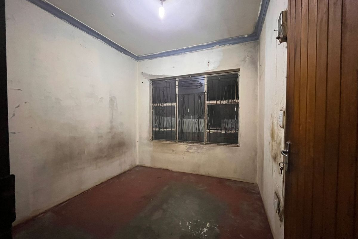 An empty bedroom featuring security bars on the window, requiring significant renovation and cosmetic updates to restore the space.