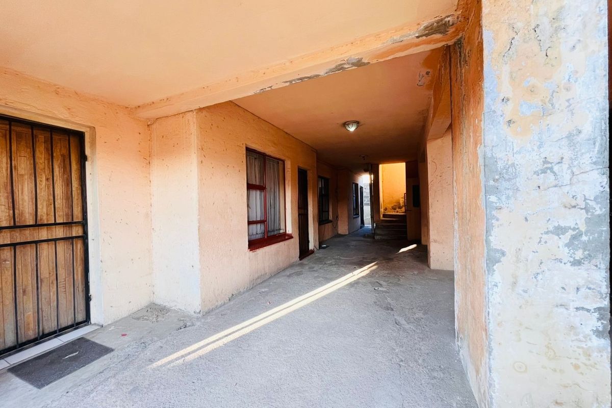 A covered outdoor walkway or patio area featuring concrete flooring and security gates, requiring maintenance and cosmetic updates to the exterior wall finishes.