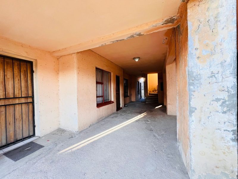 A covered outdoor walkway or patio area featuring concrete flooring and security gates, requiring maintenance and cosmetic updates to the exterior wall finishes.