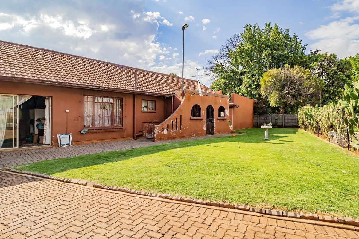 Rear view of the property featuring a paved patio area, a well-maintained lawn, and a secure boundary wall with established garden greenery.