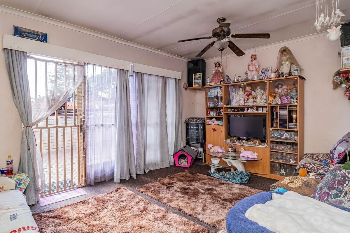A living room featuring a ceiling fan and a sliding glass door with an integrated security gate, providing access to the exterior.