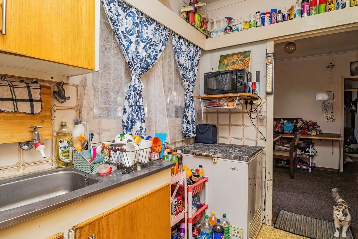 A compact kitchen area featuring dated laminate cabinetry, a stainless steel sink, and tiled splashbacks, offering potential for modernization.