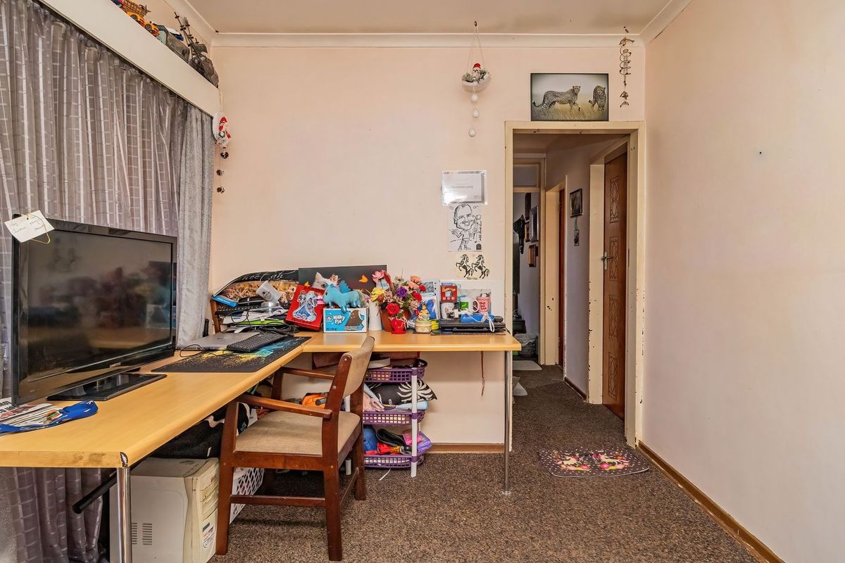 A bedroom space featuring carpeted flooring and access to an internal hallway, currently utilized as a home office area.