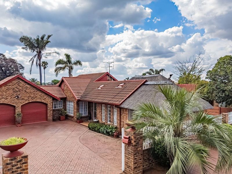 Front exterior view of a brick house featuring a double garage, paved driveway, and a combination of tiled and thatched roofing.