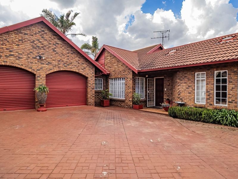 Front elevation of a face brick house featuring a double garage, tiled roof, and a spacious paved driveway entrance.