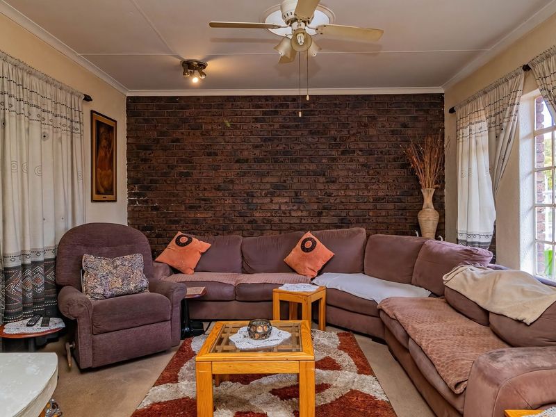 A cozy living room featuring a prominent exposed brick feature wall, a ceiling fan, and natural light through side windows.