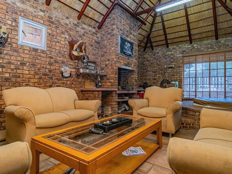 Rustic living room featuring exposed brick walls, a traditional thatched roof with timber rafters, and a built-in brick fireplace.