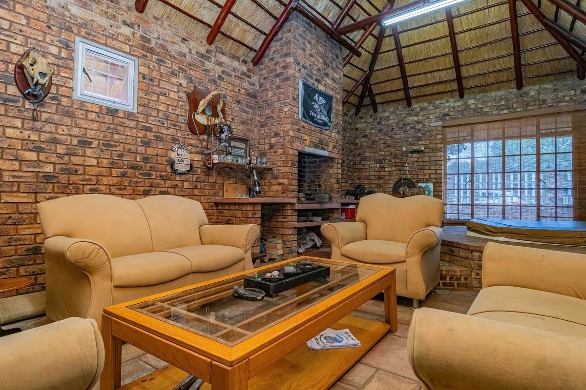 Rustic living room featuring exposed brick walls, a traditional thatched roof with timber rafters, and a built-in brick fireplace.