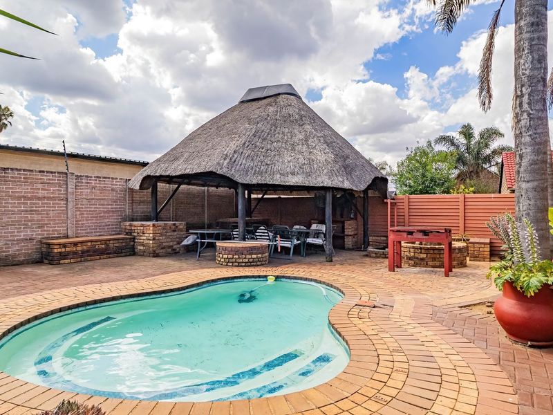 Outdoor entertainment area featuring a swimming pool, brick paving, and a traditional thatched lapa with a built-in braai.