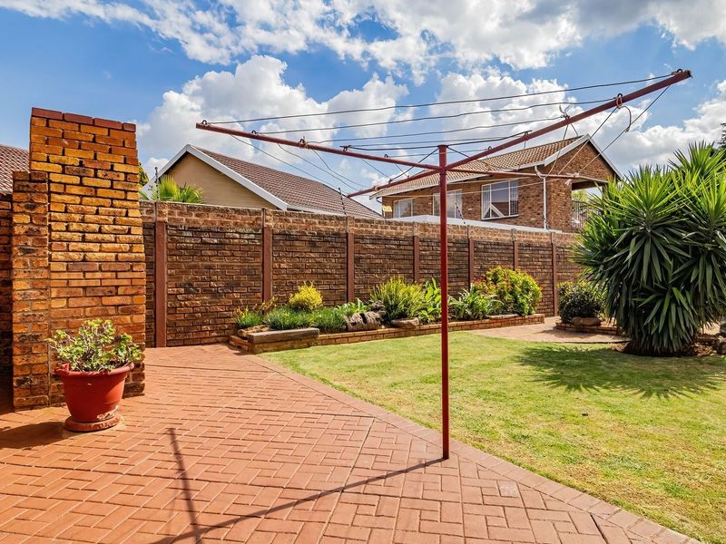 A well-maintained rear garden featuring brick paving, a raised garden bed, and a secure brick boundary wall.
