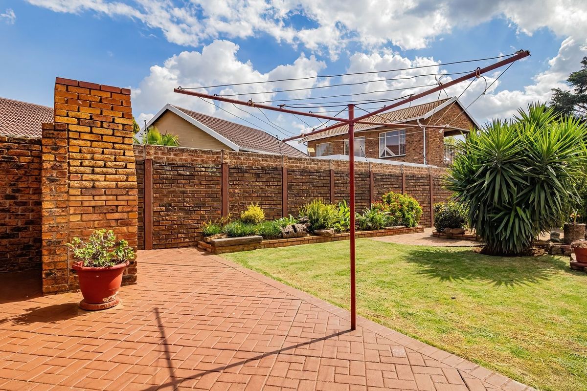 A well-maintained rear garden featuring brick paving, a raised garden bed, and a secure brick boundary wall.