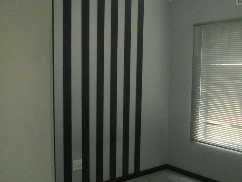 An empty bedroom featuring a striped accent wall, tiled flooring, and fitted venetian blinds.