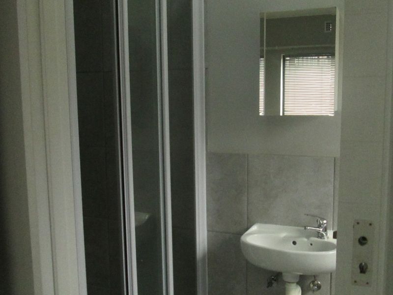 A functional bathroom featuring a shower enclosure, wall-mounted basin with mixer tap, and a mirror, presented in a clean, neutral finish.