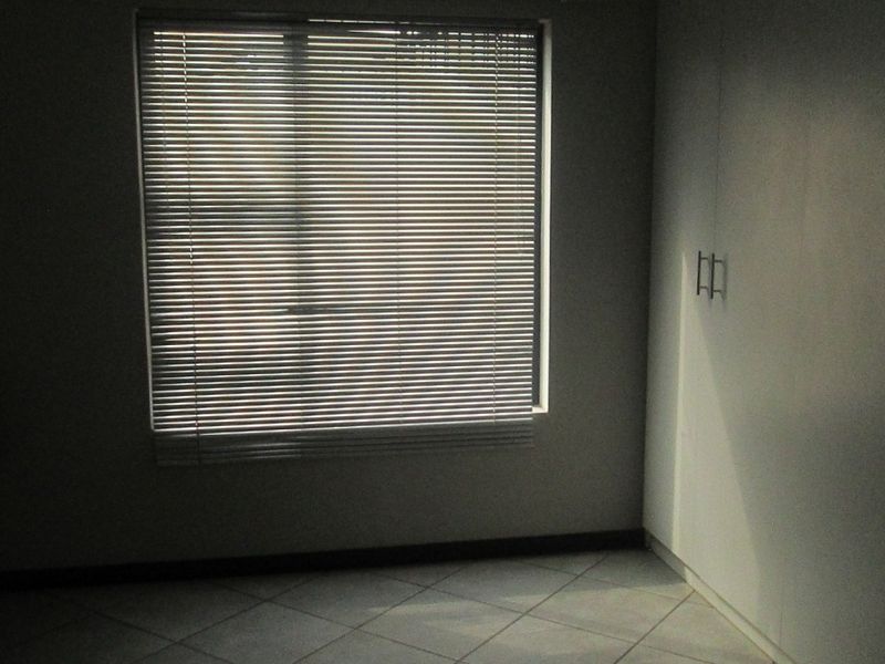 An empty bedroom featuring tiled flooring, built-in cupboards, and a window fitted with venetian blinds.