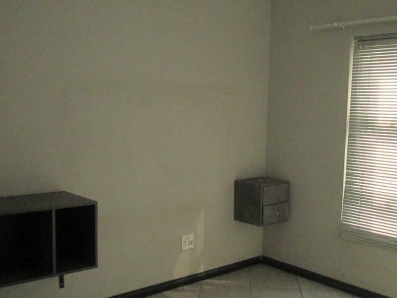 A simple bedroom featuring tiled flooring, wall-mounted storage units, and venetian blinds, providing a neutral space ready for personalization.