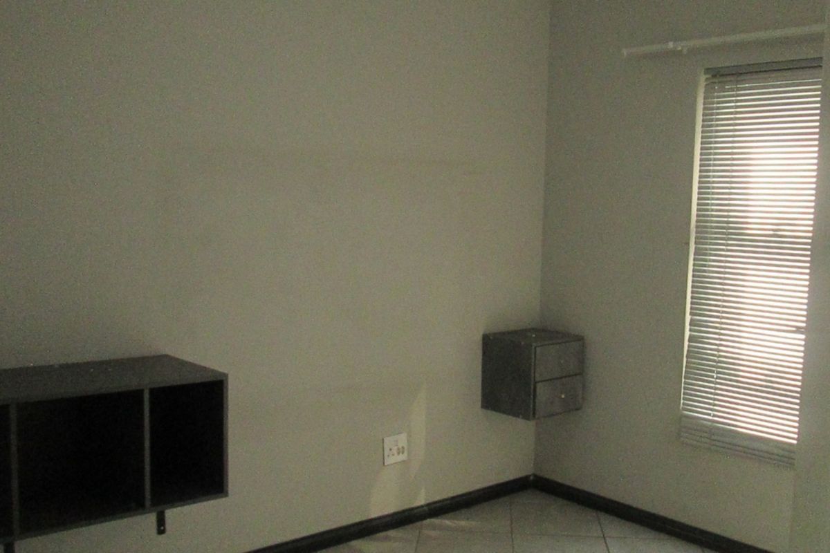 A simple bedroom featuring tiled flooring, wall-mounted storage units, and venetian blinds, providing a neutral space ready for personalization.