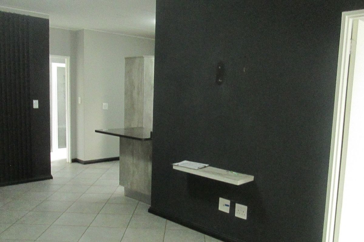 An open-plan living area featuring tiled flooring, a built-in breakfast bar, and a dark accent wall with a mounted shelf.